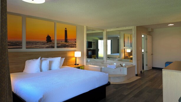 Une chambre d’hôtel dotée d’un grand lit, d’un coin salon avec vue sur la mer, et d’une salle de bain avec baignoire et miroir.