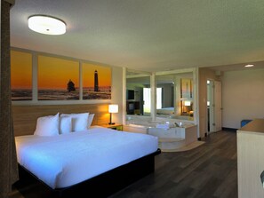 A hotel room with a large bed, a sitting area with a view of the sea, and a bathroom with a bathtub and mirror. - Days Inn & Suites by Wyndham Port Huron (Port Huron)