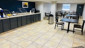 Une cuisine d’hôtel avec un buffet, un sol carrelé et un espace détente avec des tables et des chaises.