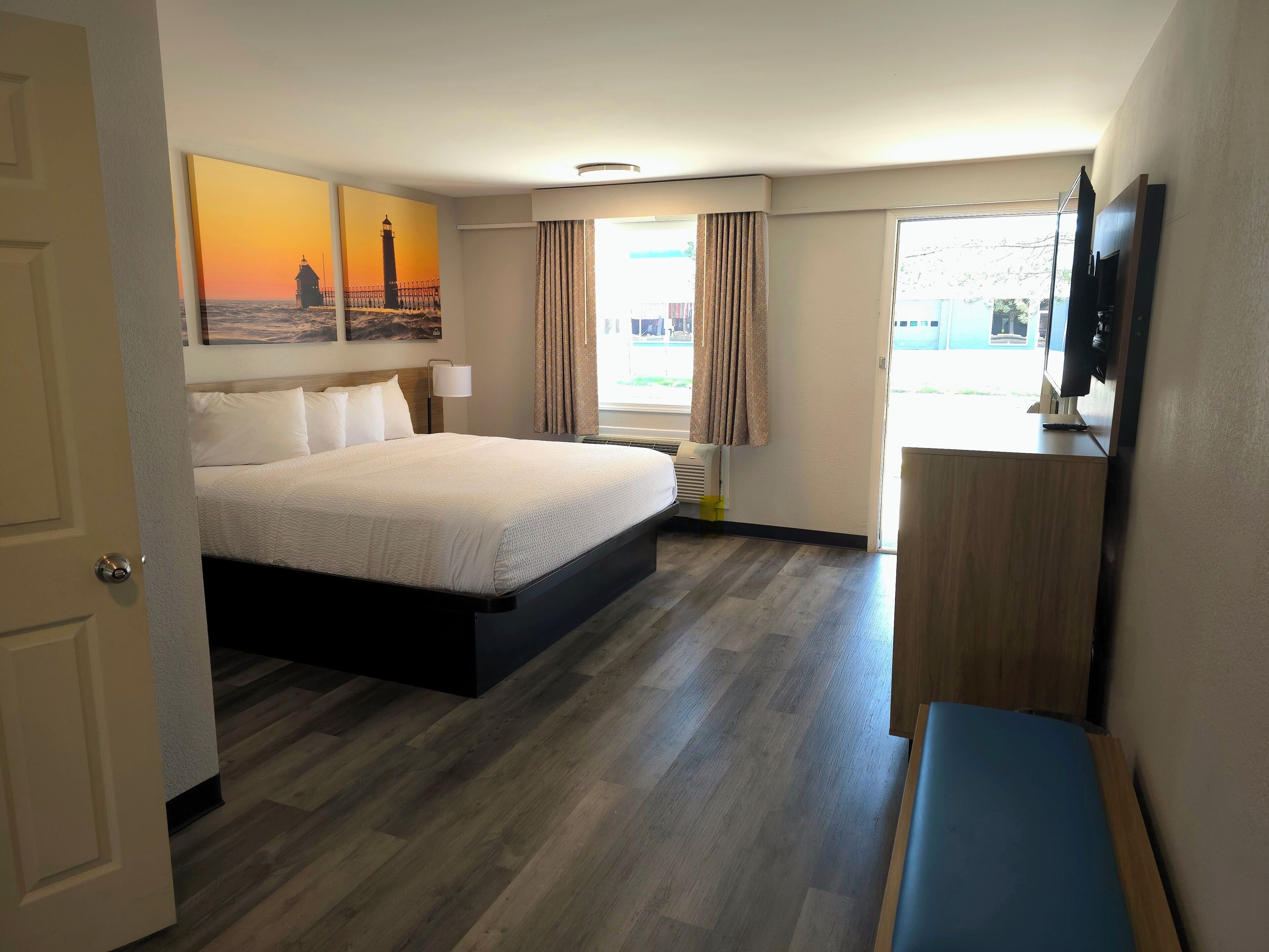 A hotel room with a bed, a desk, a television, and a window with curtains.