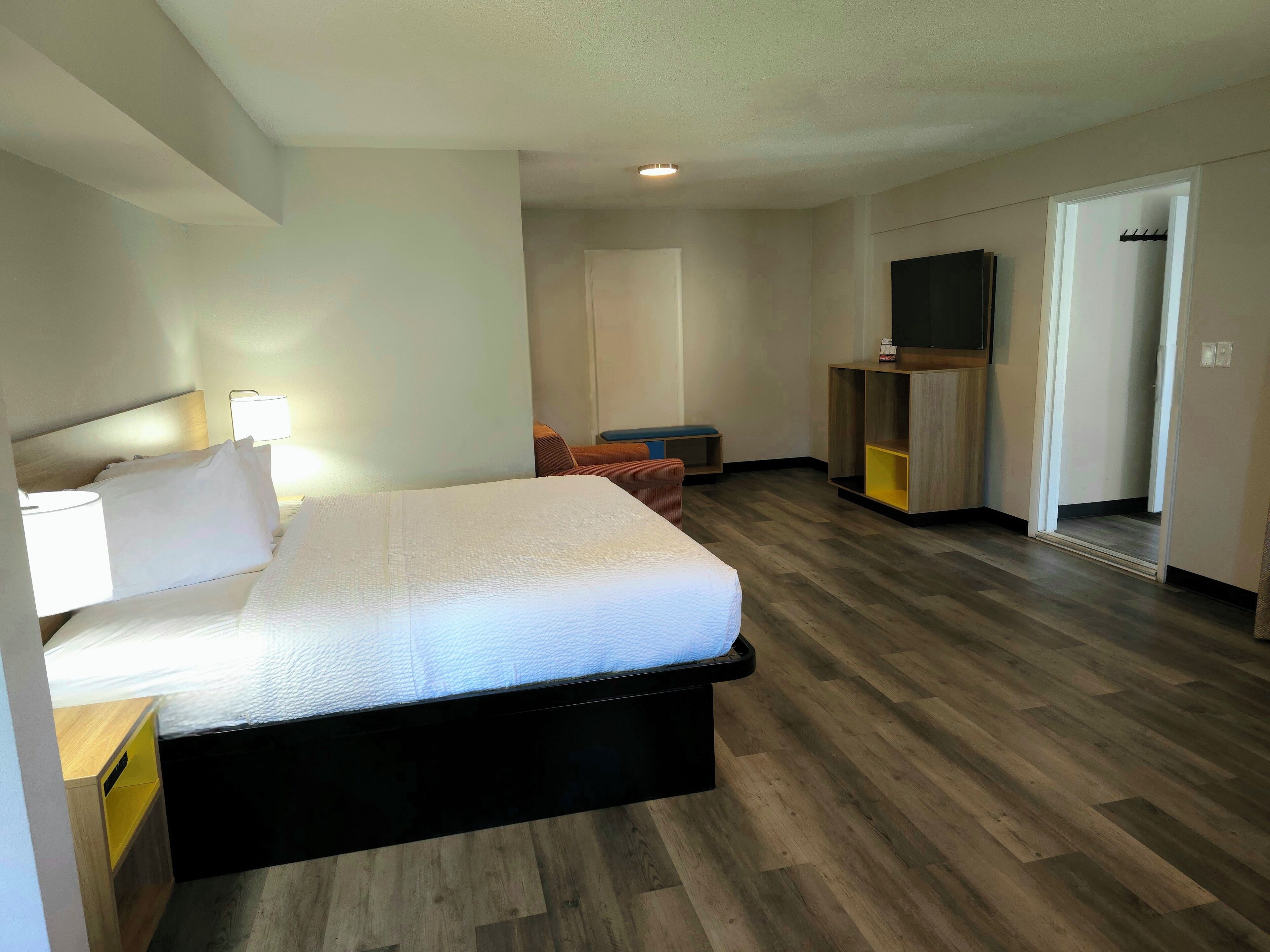 A hotel room with a bed, bedside table, lamp, and a TV on a stand.
