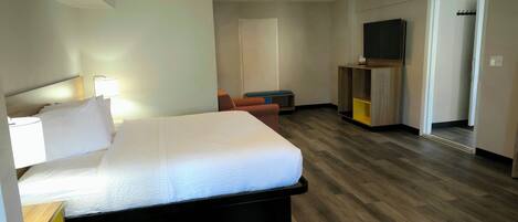 A hotel room with a bed, bedside table, lamp, and a TV on a stand.