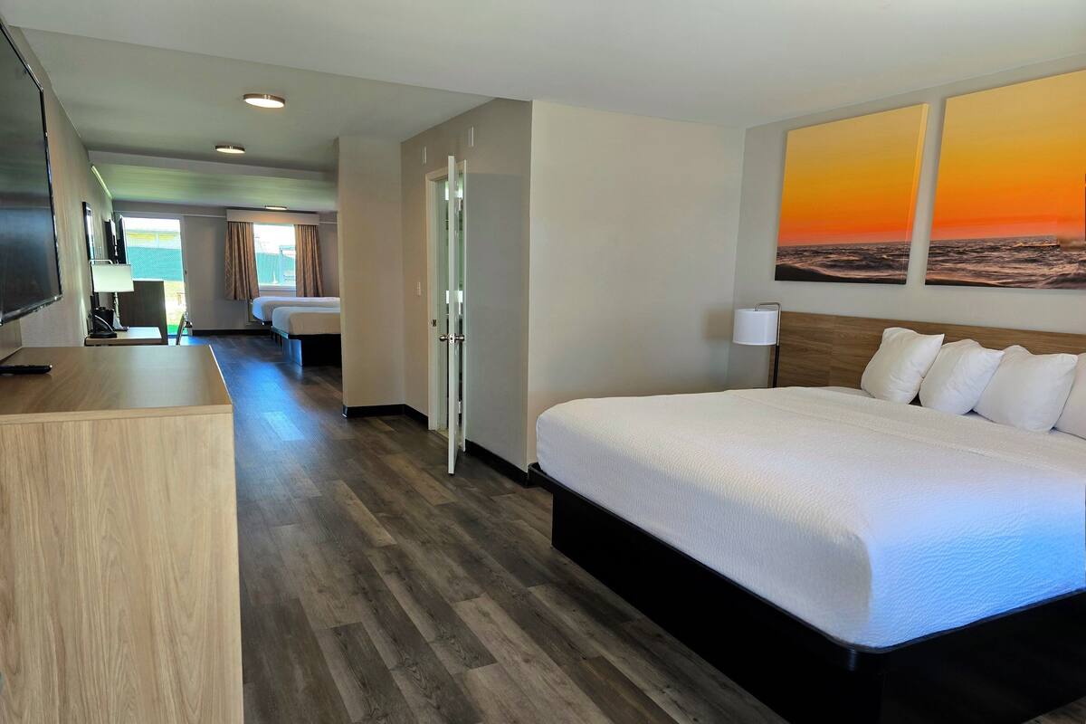A hotel room with a large bed, a desk, a TV, and a painting of a sunset.