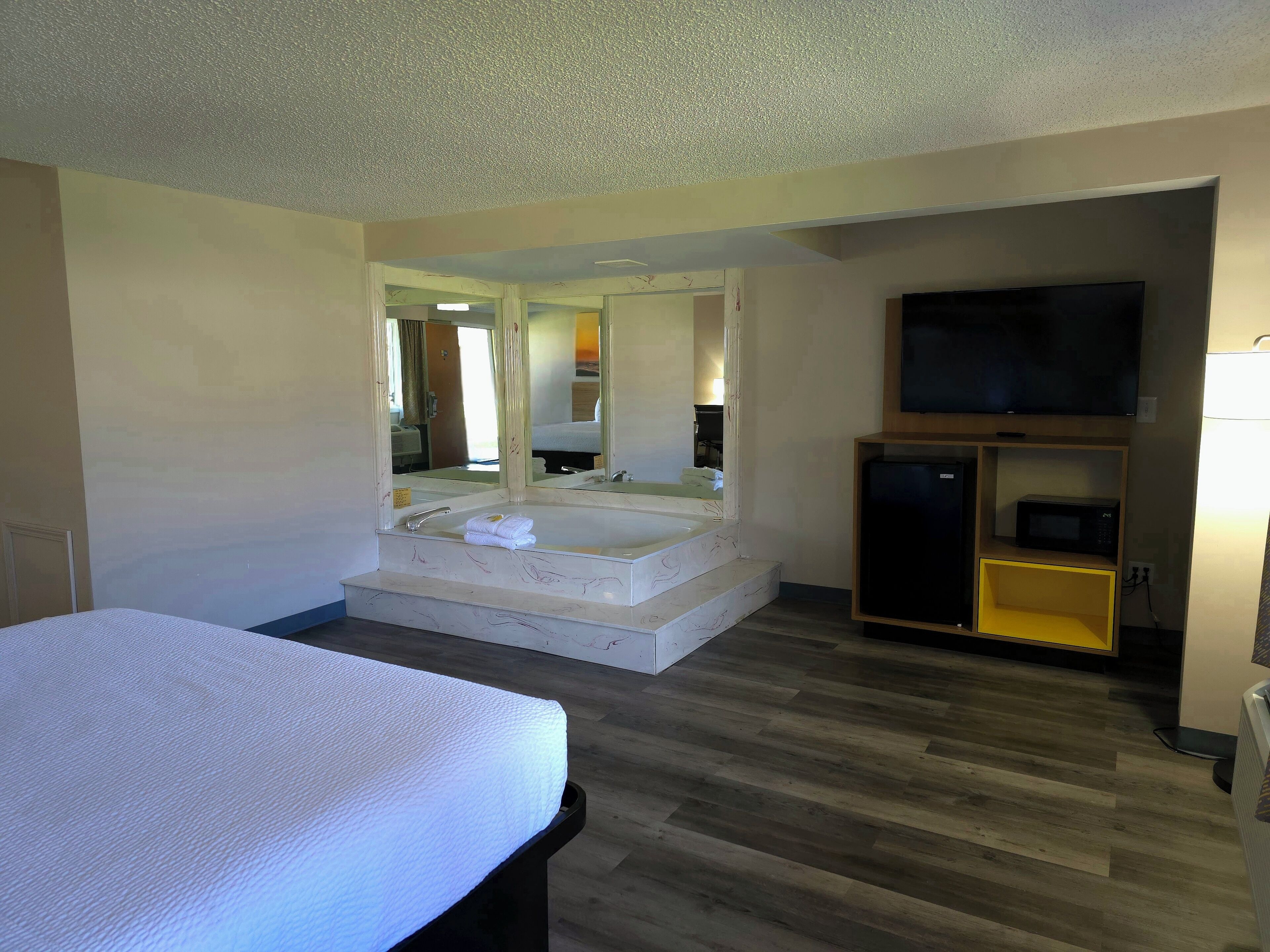 A hotel room with a large bed, a bathroom with a bathtub, a TV, and a microwave.