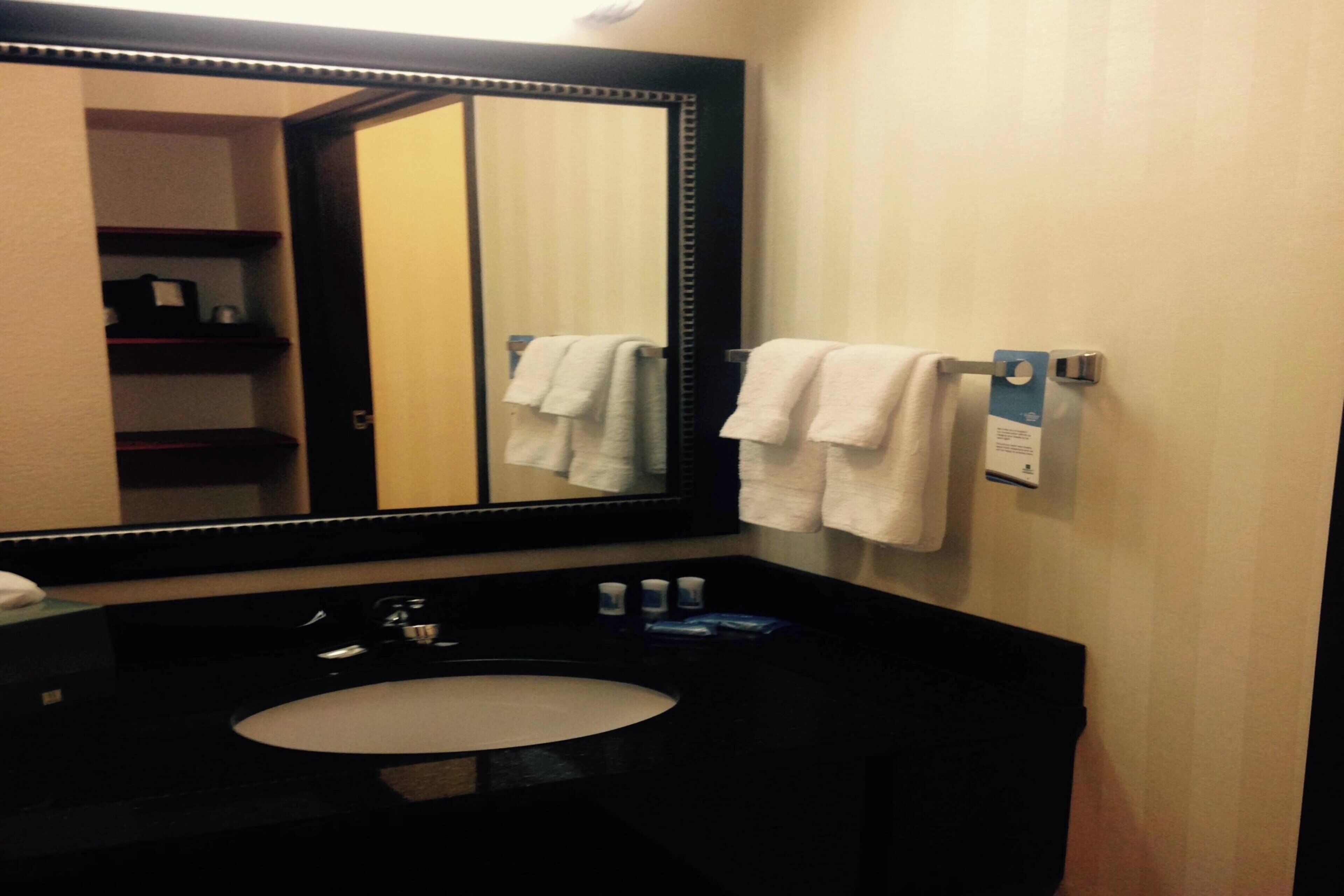 A bathroom with a large mirror, a black sink, and two white towels hanging on a towel rack.