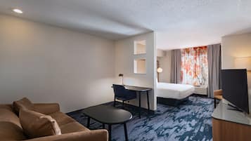 Habitación de hotel con sofá, escritorio, cama, televisor y ventana con cortinas.