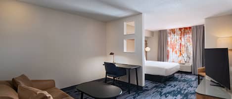 A hotel room with a sofa, a desk, a bed, a TV, and a window with curtains.