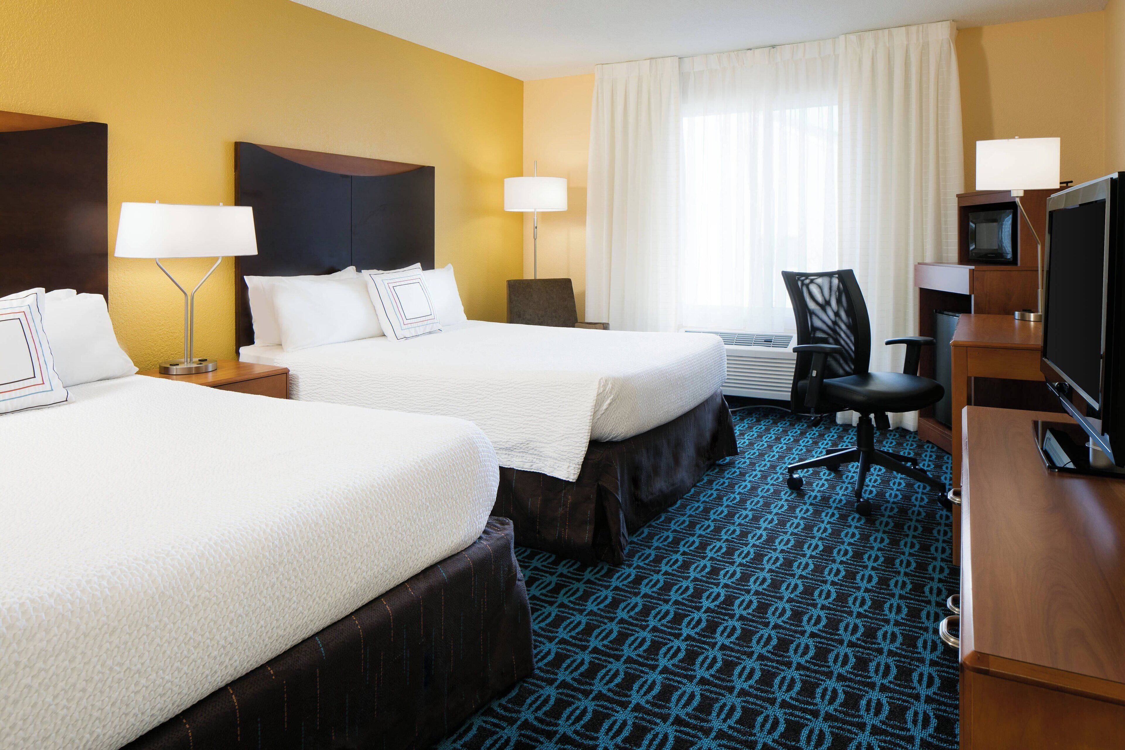 A hotel room with two beds, a desk with a TV, and a chair.