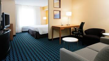 A hotel room with a bed, desk, two chairs, a TV, and a lamp.