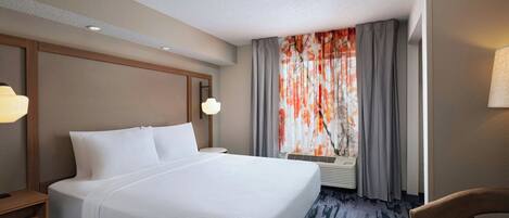Habitación de hotel con una cama grande, una silla, una mesita de noche, una lámpara y una ventana con cortinas.