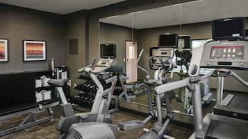 Un gimnasio con varios equipos de ejercicio, incluyendo cintas de correr y elípticas, y un letrero motivacional en la pared.