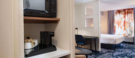 A hotel room with a microwave, coffee maker, and a bed.