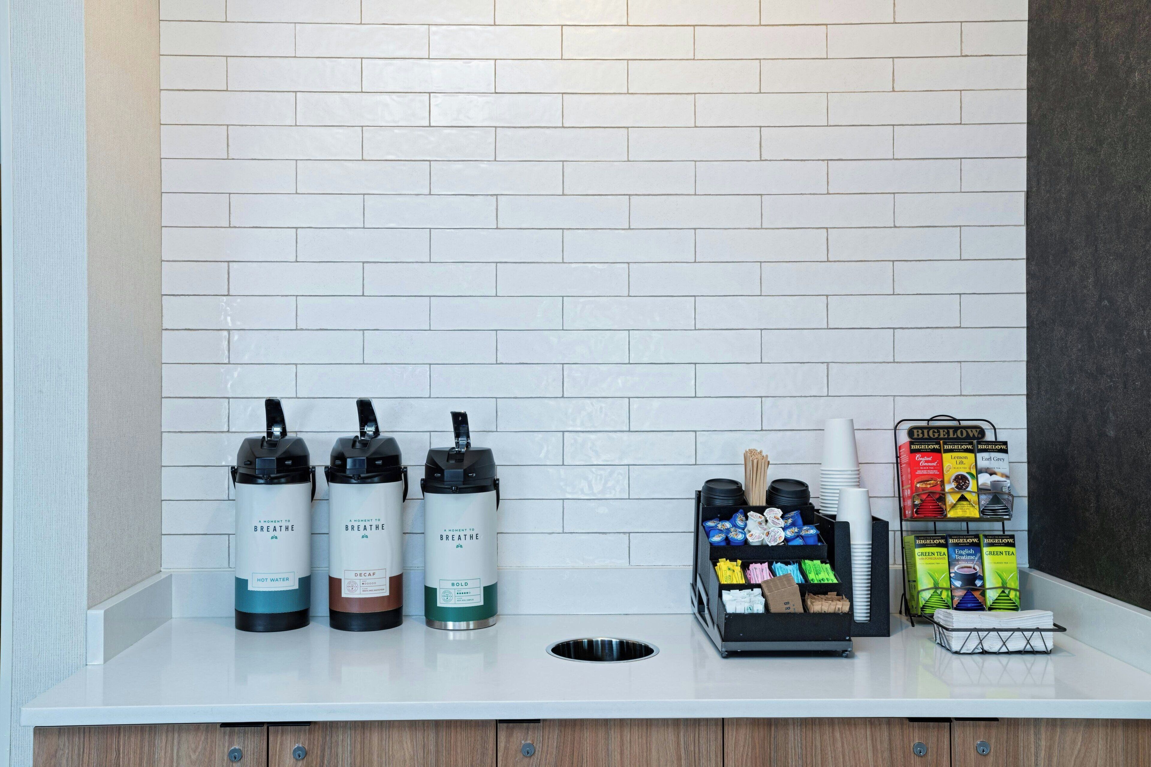 Una mesa de mostrador con dispensadores de agua, una máquina de café y una exhibición de productos de té y café.