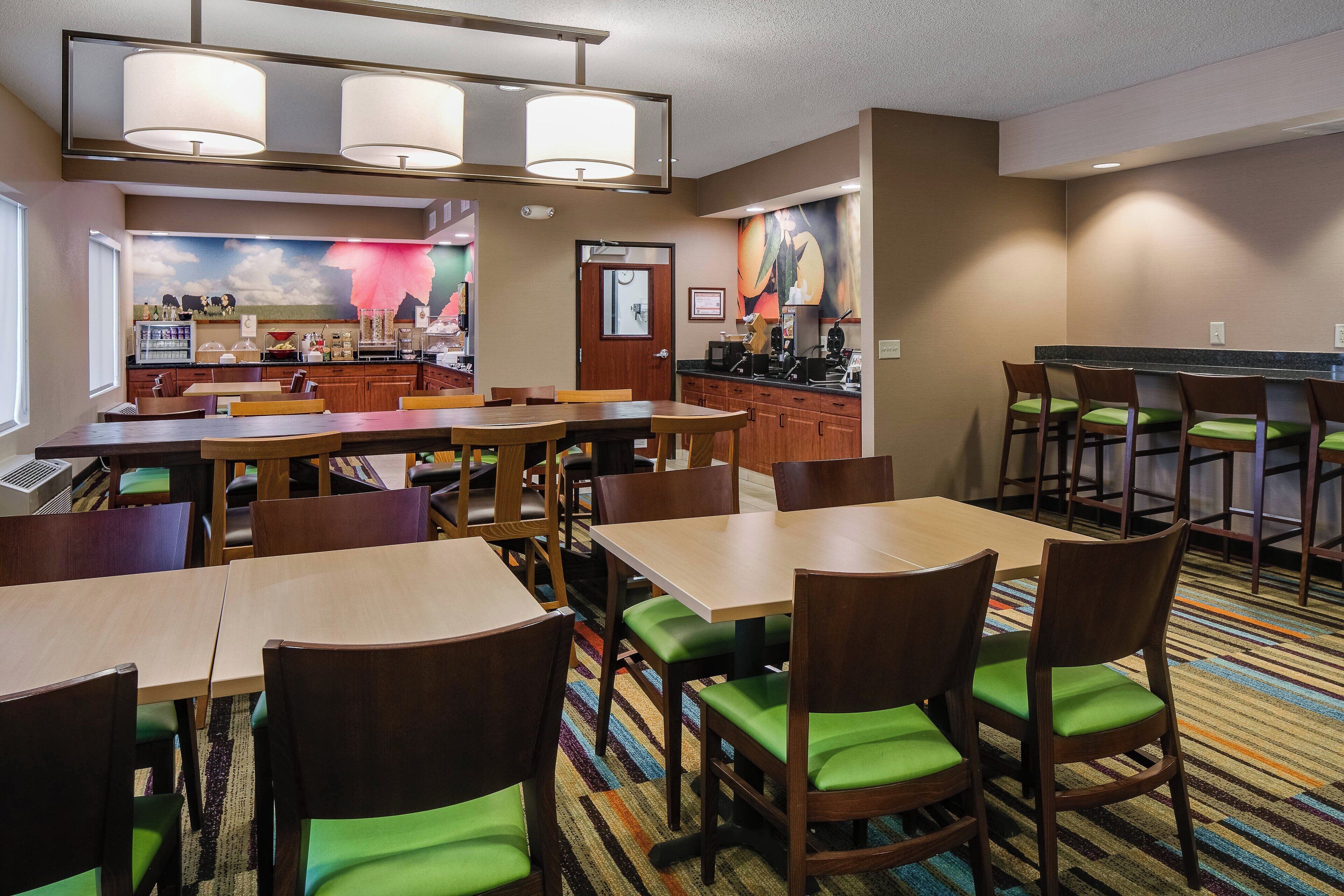 Een restaurantgedeelte in een hotel met meerdere tafels, stoelen, een bar en een keuken.