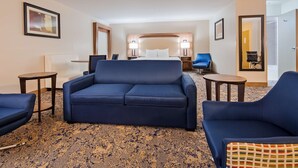 A hotel room with a large sofa, two armchairs, a small table, a bed with a wooden headboard, and a carpeted floor. - Best Western Plus Kansas City Airport-KCI East (Kansas City)