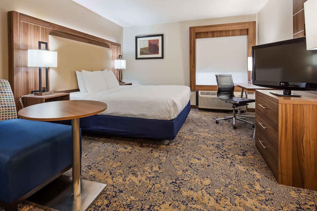 A hotel room with a bed, a desk with a chair, a television, a small table, and a sofa.