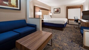 A hotel room with a blue sofa, a wooden table, a bed with white bedding, a desk with a television, and two wall-mounted lamps. - Best Western Plus Kansas City Airport-KCI East (Kansas City)