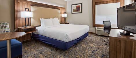 A hotel room with a bed, bedside tables, a desk with a chair, a television, and a window.