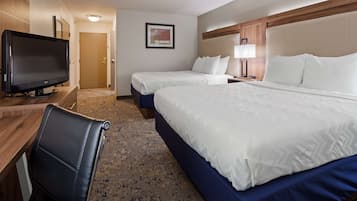 A hotel room with a large bed, a smaller bed, a desk with a flat-screen TV, a leather chair, and a carpeted floor.