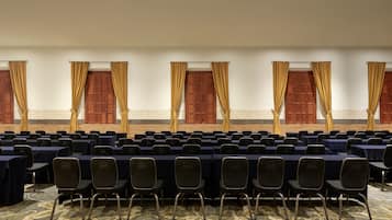 A conference room with rows of tables and chairs, large windows with curtains, and a patterned carpet.