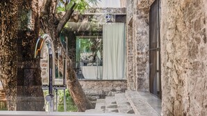 Ein Badezimmer mit Stehwänden, einer Badewanne, einem Fenster mit Vorhängen und einem Baum vor der Fensterfront.