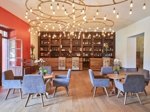 Relax in a stylish seating area with a round table and six chairs, surrounded by a unique light fixture and a bookshelf filled with decorative items.