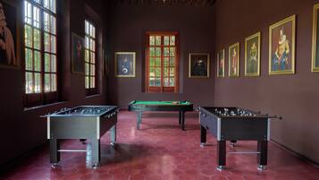 A room with three foosball tables, large windows, and several framed artworks on the walls.