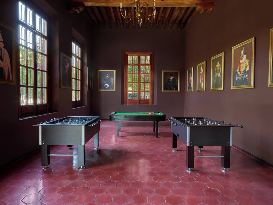 A room with three foosball tables, large windows, and several framed artworks on the walls.