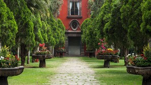 Ein Weg führt zu einem Gebäude mit roter Fassade, umgeben von üppiger Vegetation und Blumenkästen.