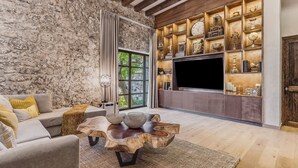 Ein modernes Wohnzimmer mit Steinwand, Holztisch, grauem Sofa und einer TV-Wand.