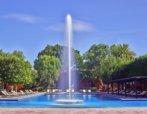 Relax by the serene pool surrounded by lounge chairs and umbrellas, with a central fountain and shaded seating area.