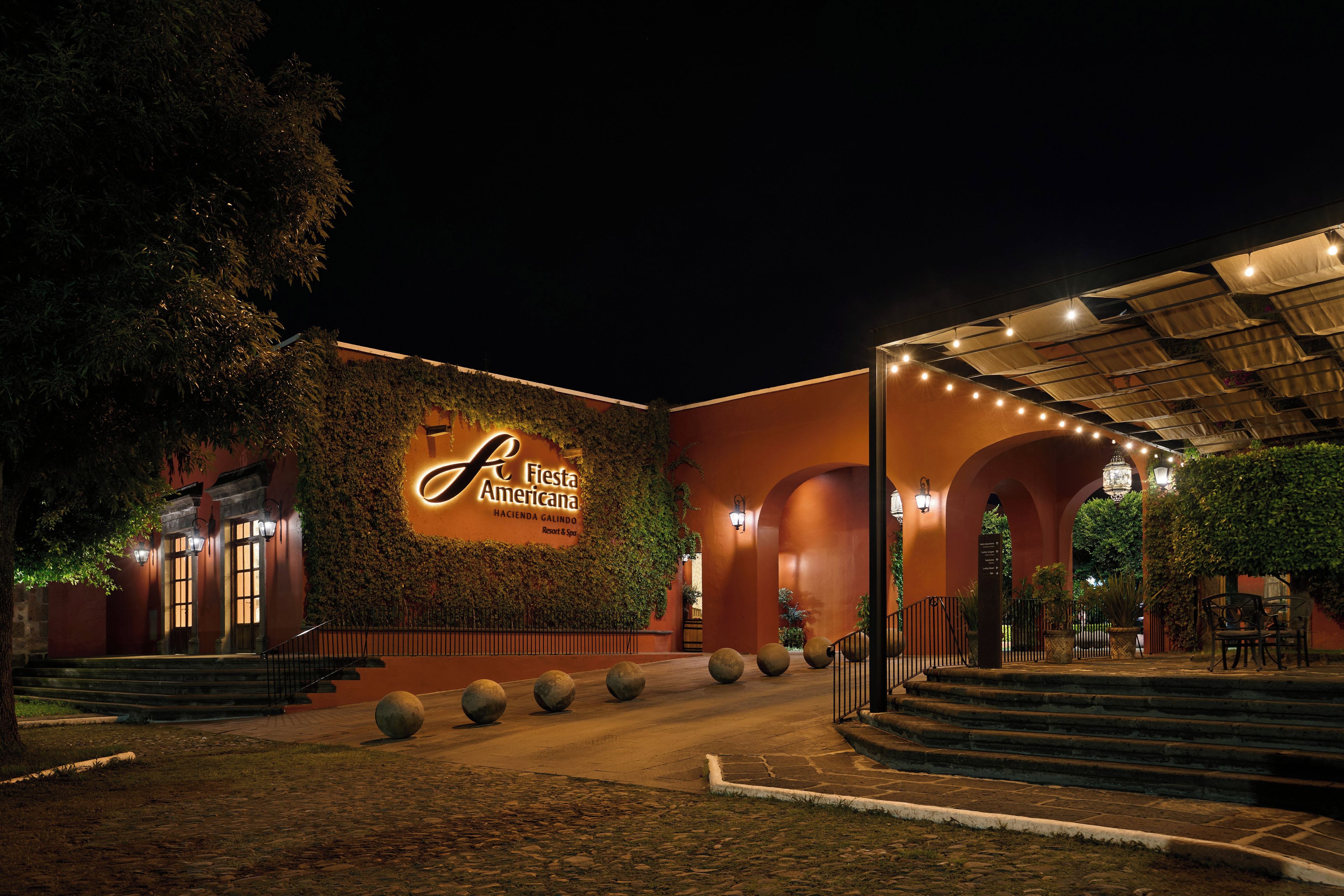 Entrada de hotel con un letrero iluminado grande, un área exterior cubierta y una escalera hacia la entrada.