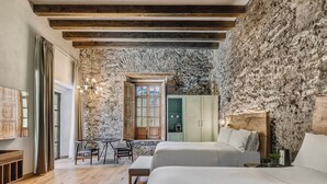 A bedroom with two beds, a stone wall, wooden beams, a window, a desk, and a chair. - Fiesta Americana Hacienda Galindo Resort & Spa (San Juan del Río)