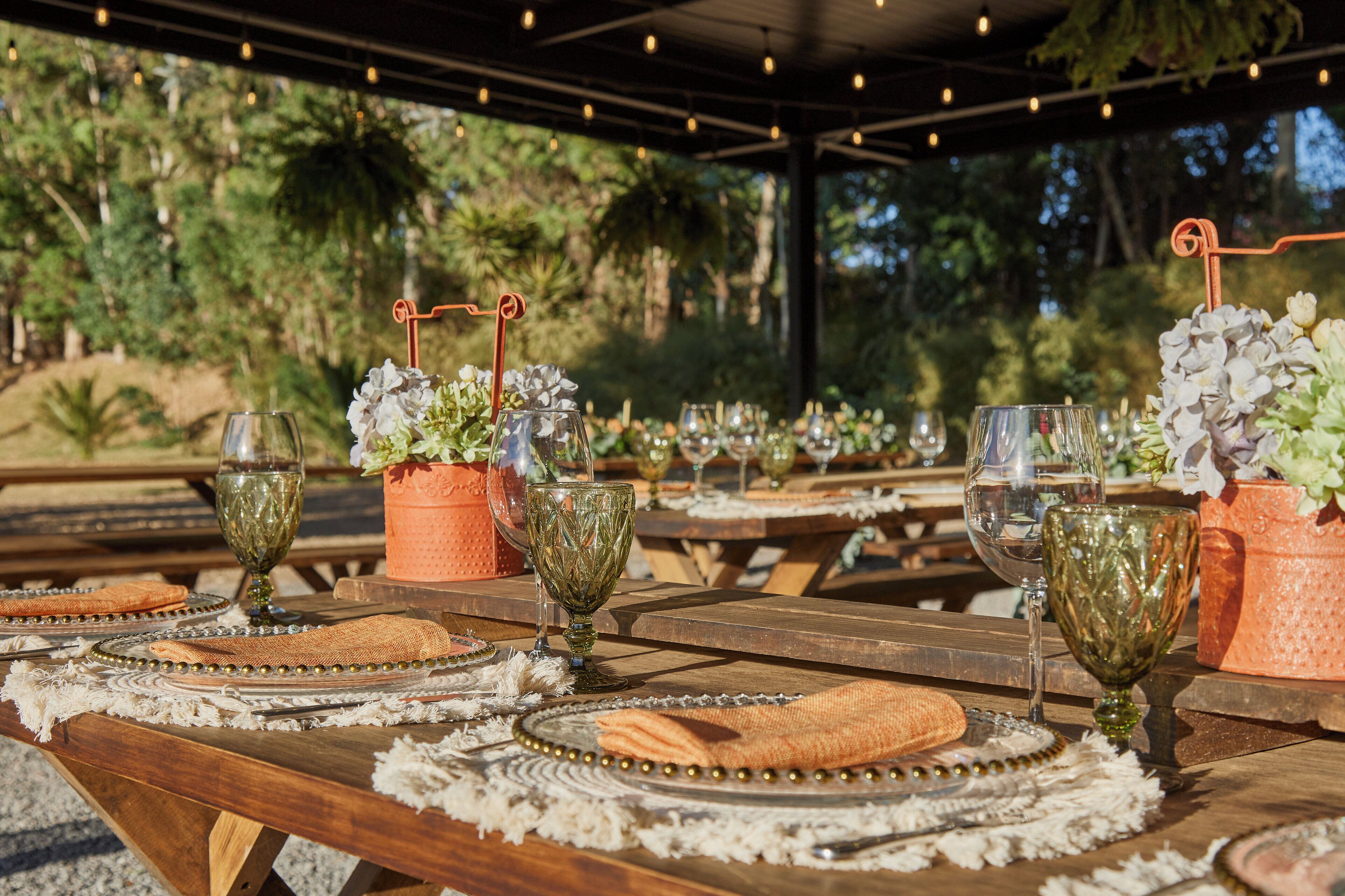 Un espace extérieur aménagé pour les repas, avec des tables en bois, de la vaisselle et des plantes en pot.