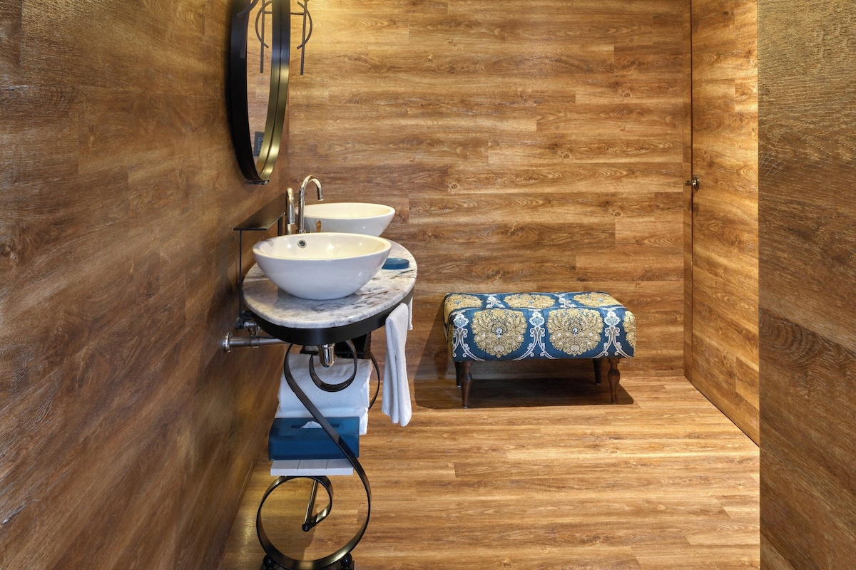 A bathroom with wooden walls, a round sink, a mirror, and a bench.