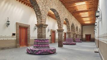 A corridor with stone arches, wooden ceiling, and patterned floor cushions.