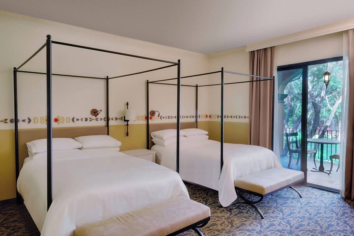 Ein Zimmer mit zwei Betten, einer Bank, einem kleinen Tisch und Blick ins Freie.