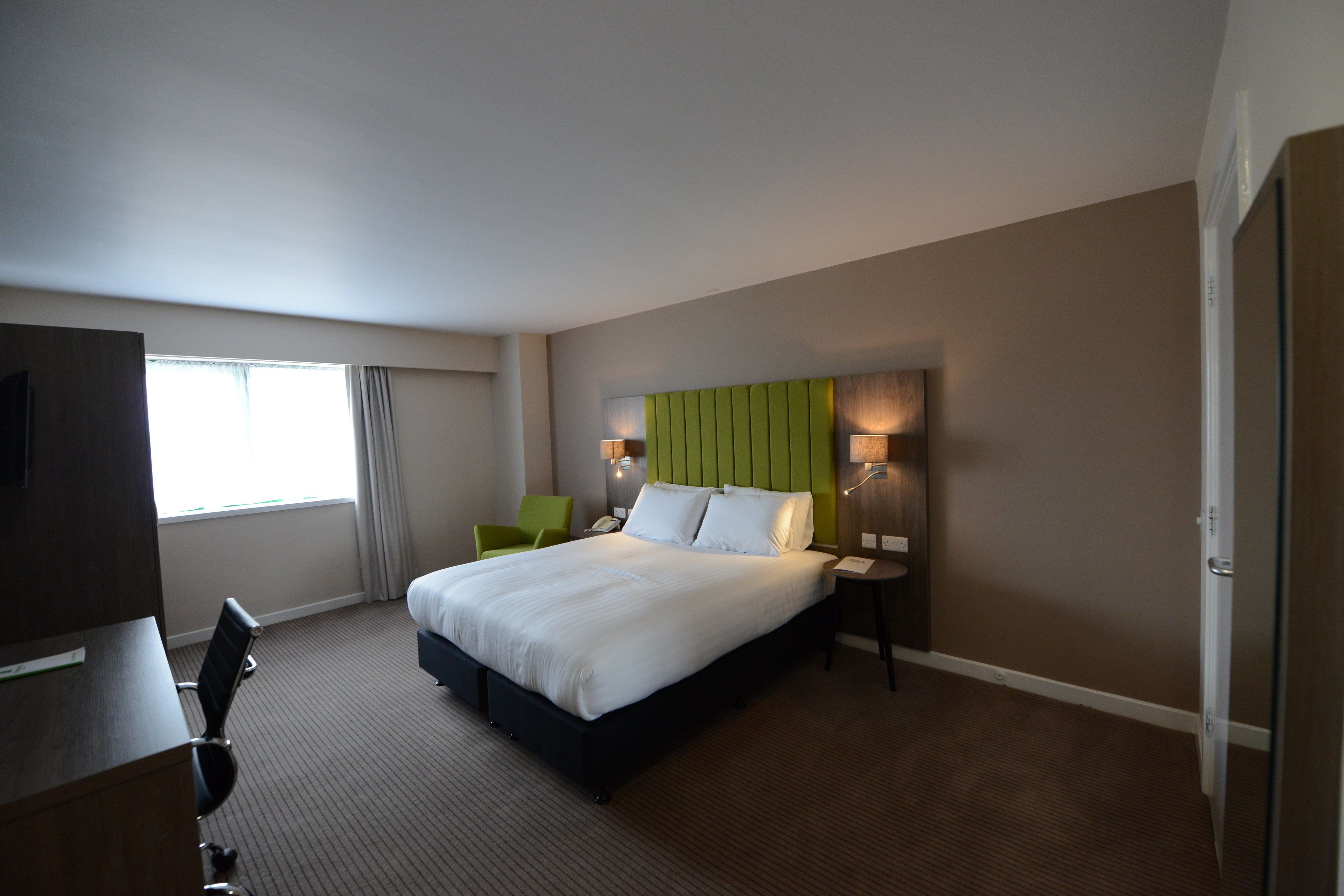 A hotel room with a large bed, a desk with a chair, a TV, and a window with curtains.