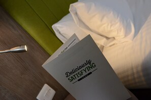 A booklet titled "Deliciously Satisfying Food" on a wooden surface next to a white pillow and a green cushion.
