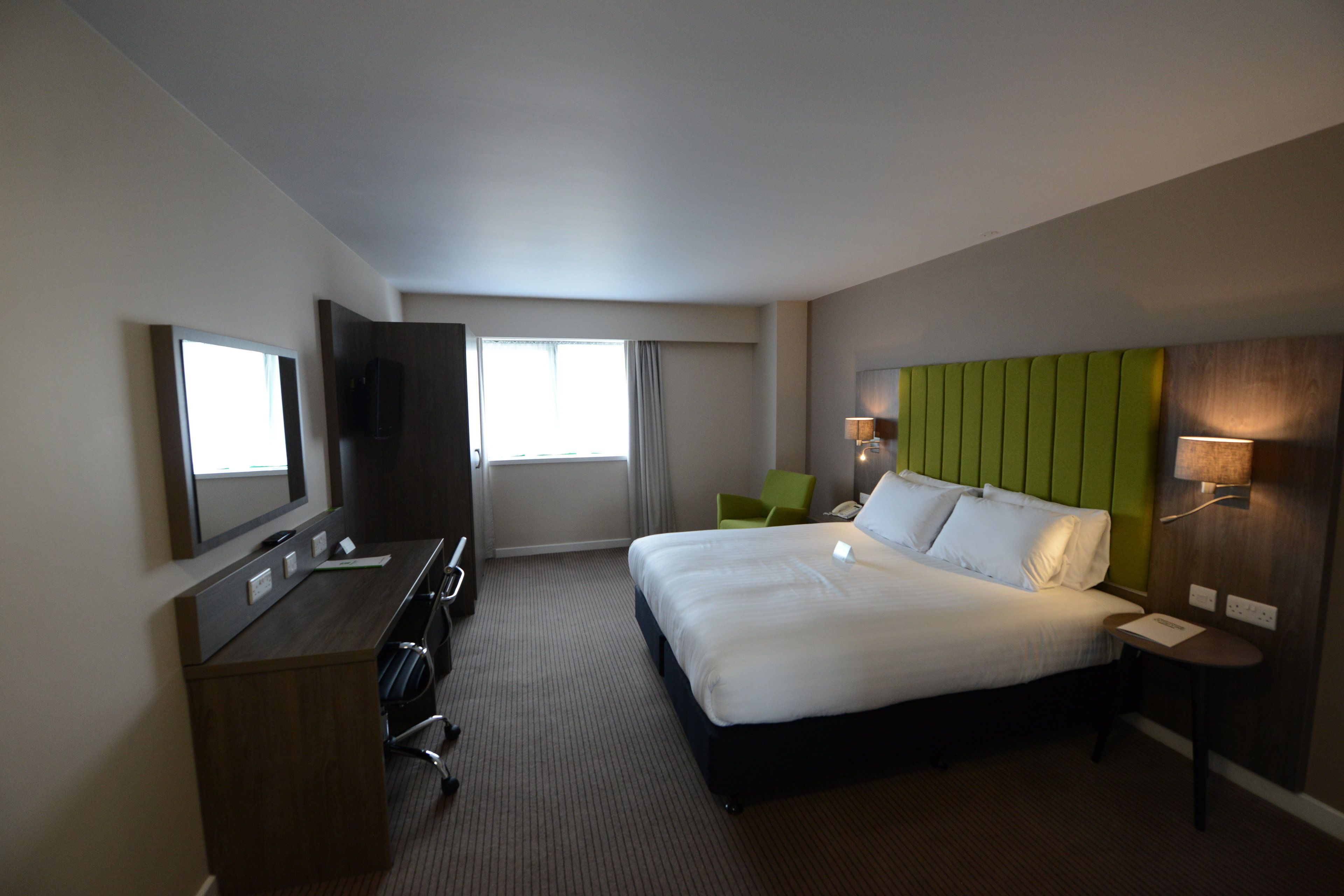 A hotel room with a large bed, a desk with a chair, a TV, and a window with curtains.