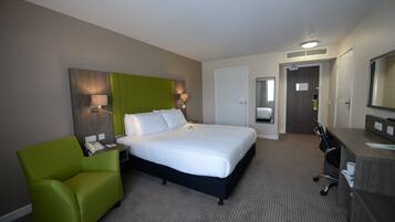 A hotel room with a bed, a green armchair, a desk with a telephone, and a mirror.