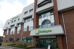 A Holiday Inn hotel with a modern facade, large windows, and a green and white color scheme.