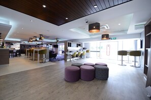 A modern hotel lobby with a bar area, seating arrangements, and a visible exit sign.