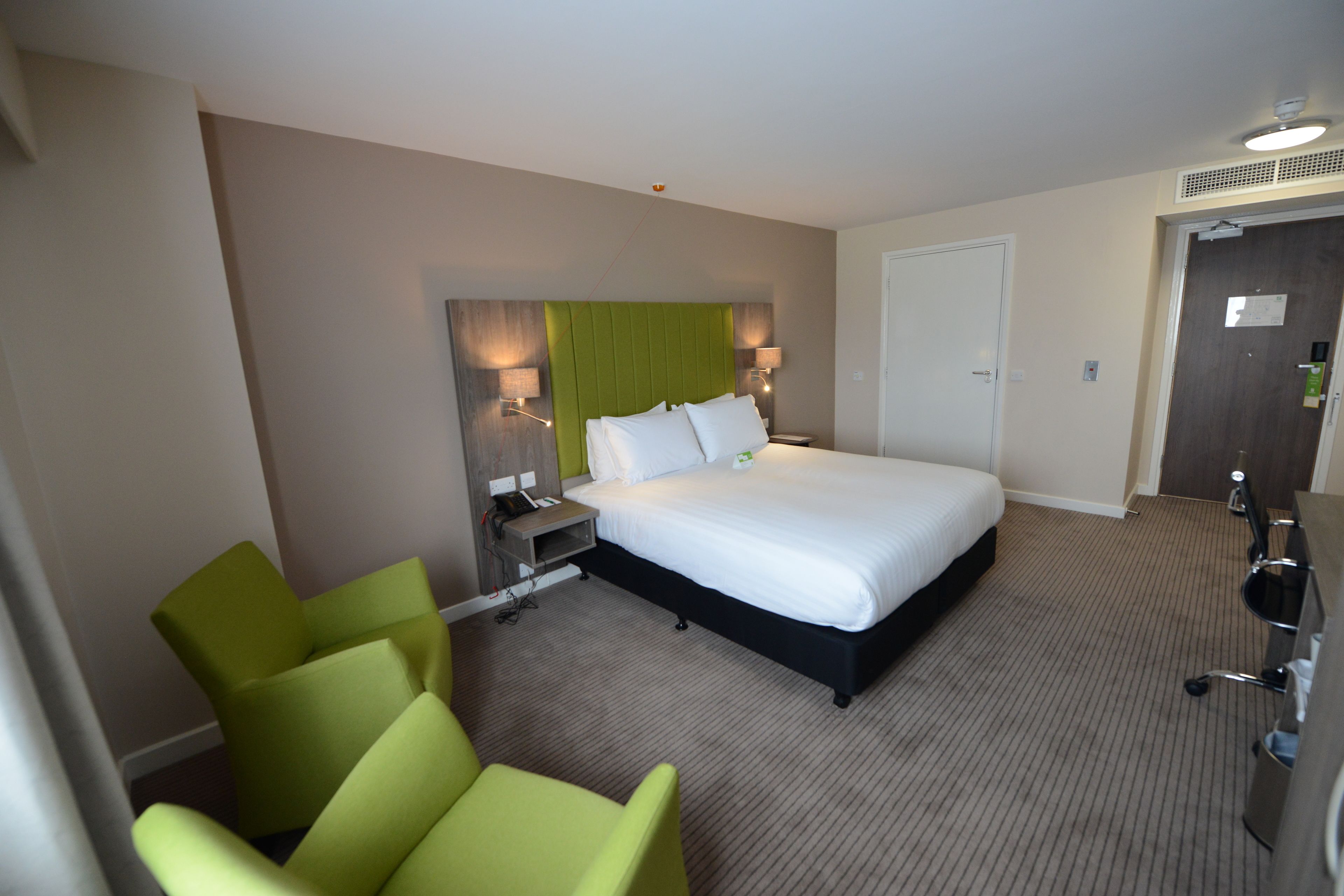 A hotel room with a large bed, a desk, a chair, and a lamp.