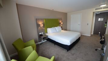A hotel room with a large bed, a desk, a chair, and a lamp.