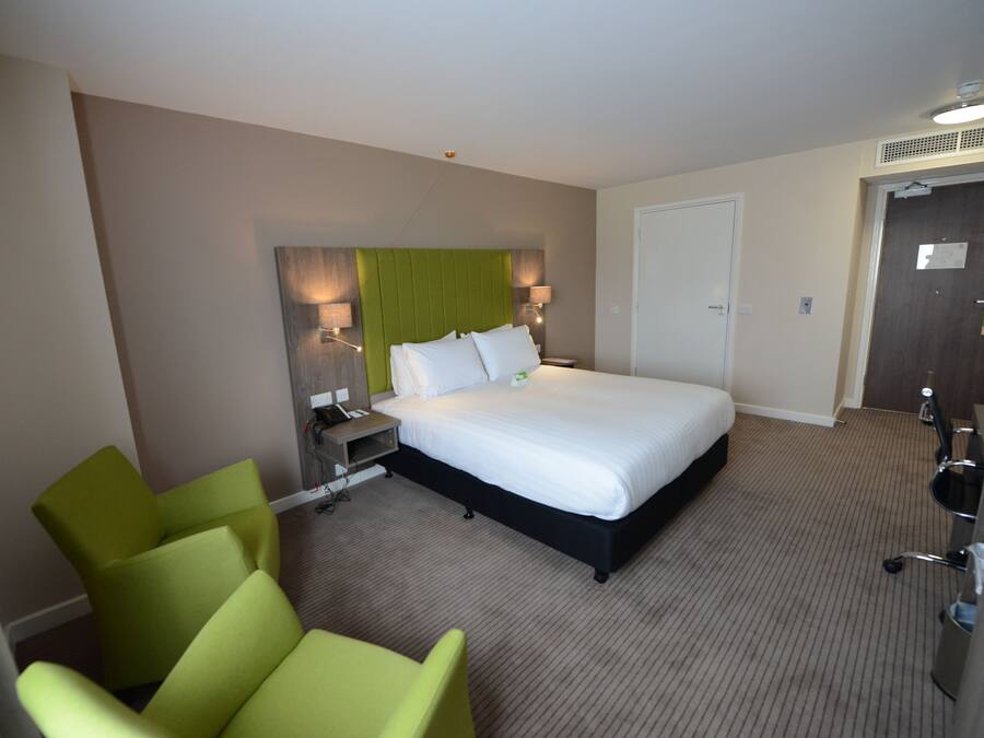 A hotel room with a large bed, a desk, a chair, and a lamp.