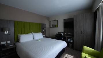A hotel room with a large bed, a green accent wall, a desk with a chair, a TV, and a wardrobe.