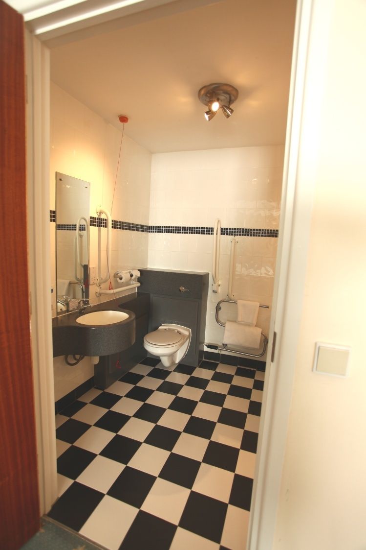 A bathroom with a black and white checkered floor, a white toilet, a sink, and a shower area.