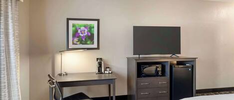 A hotel room with a bed, a desk with a chair, a television, a coffee maker, and a microwave.