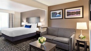 Quarto de hotel com cama, sofá, mesa de centro e duas imagens emolduradas na parede.